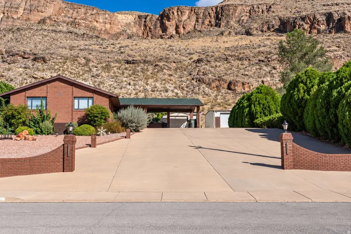 Brick exterior with a covered carport, concrete driveway, and established landscaping with mature shrubs