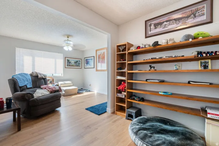 Wood-finish flooring throughout, ceiling fan with light fixture, ample natural light from window, built-in wooden shelving, and recessed wall opening