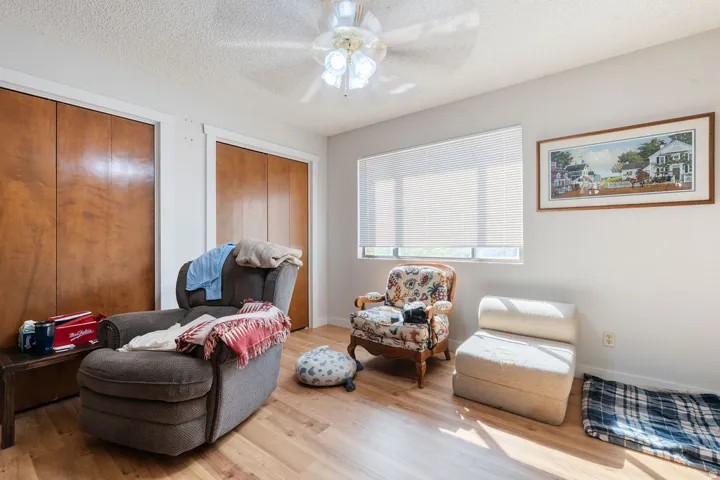 Wood-finish flooring, two wood-paneled closet doors, ceiling fan, and a single window with blinds