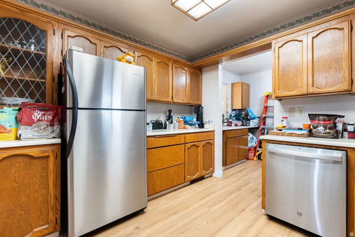 Wood-finish flooring, wood cabinetry with decorative glass inserts, stainless steel refrigerator, and stainless steel dishwasher