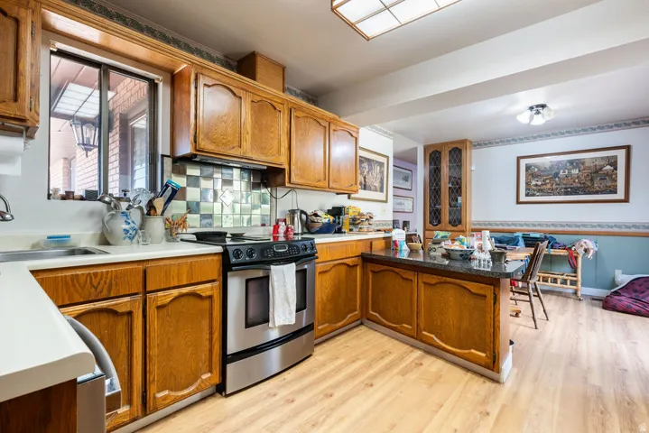Wood-finish flooring, wood cabinetry with decorative trim, stainless steel range, built-in display cabinet, and checkerboard tile backsplash