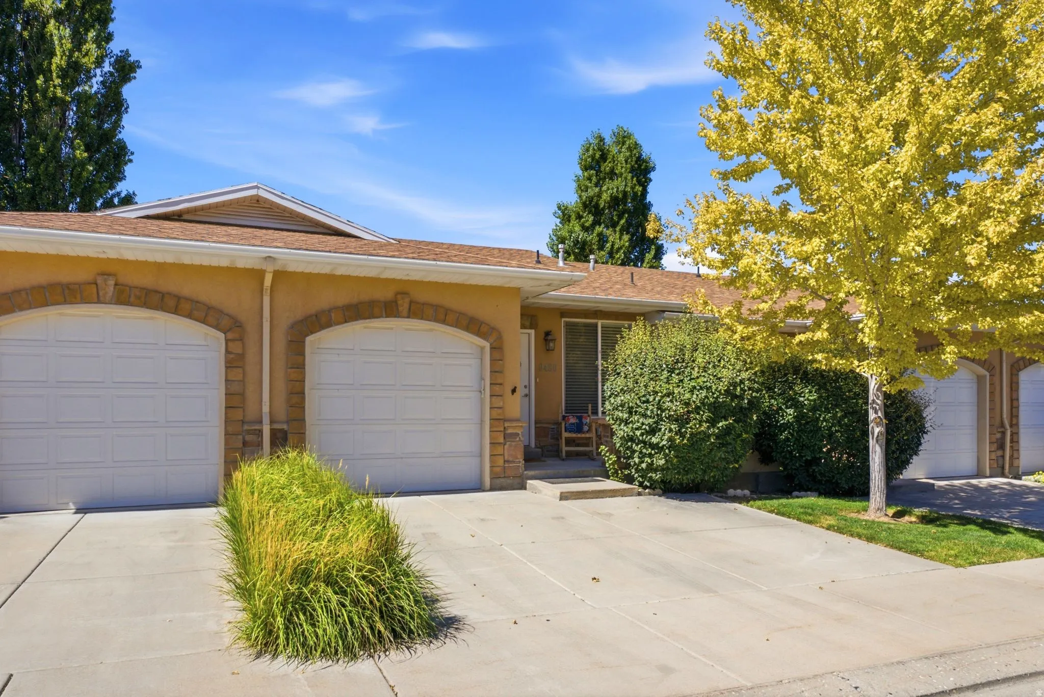 Stucco exterior with stone accents, two white garage doors, and concrete driveway