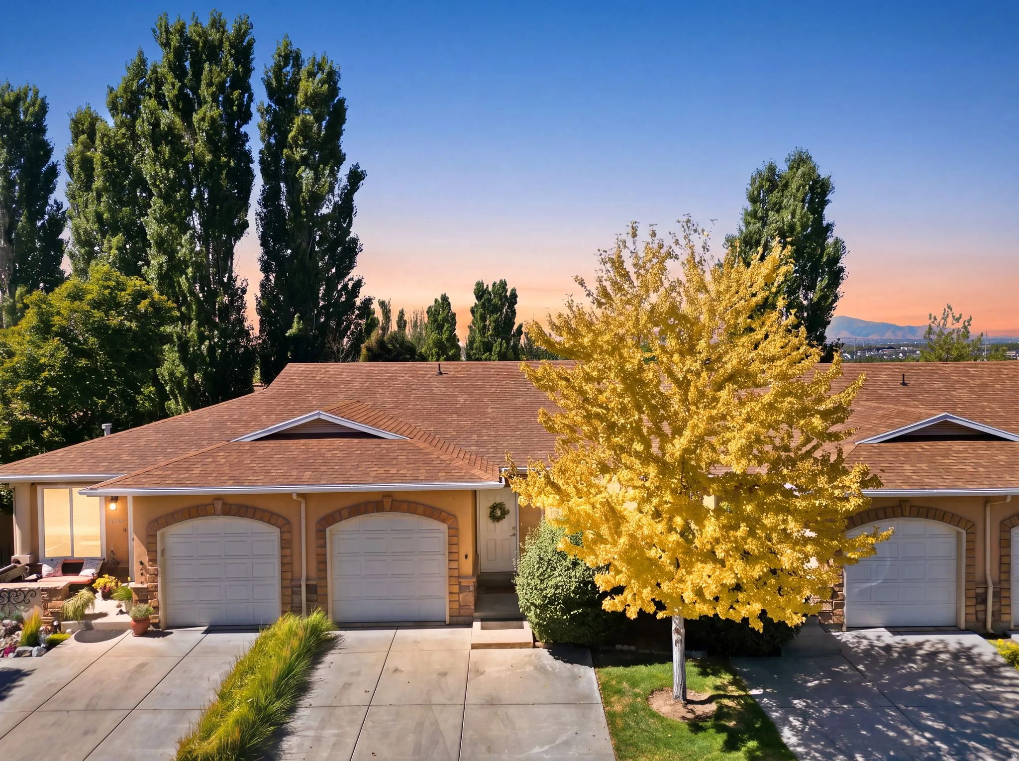 Exterior features a light-toned stucco facade with stone accents, arched garage door openings, and a brown shingle roof