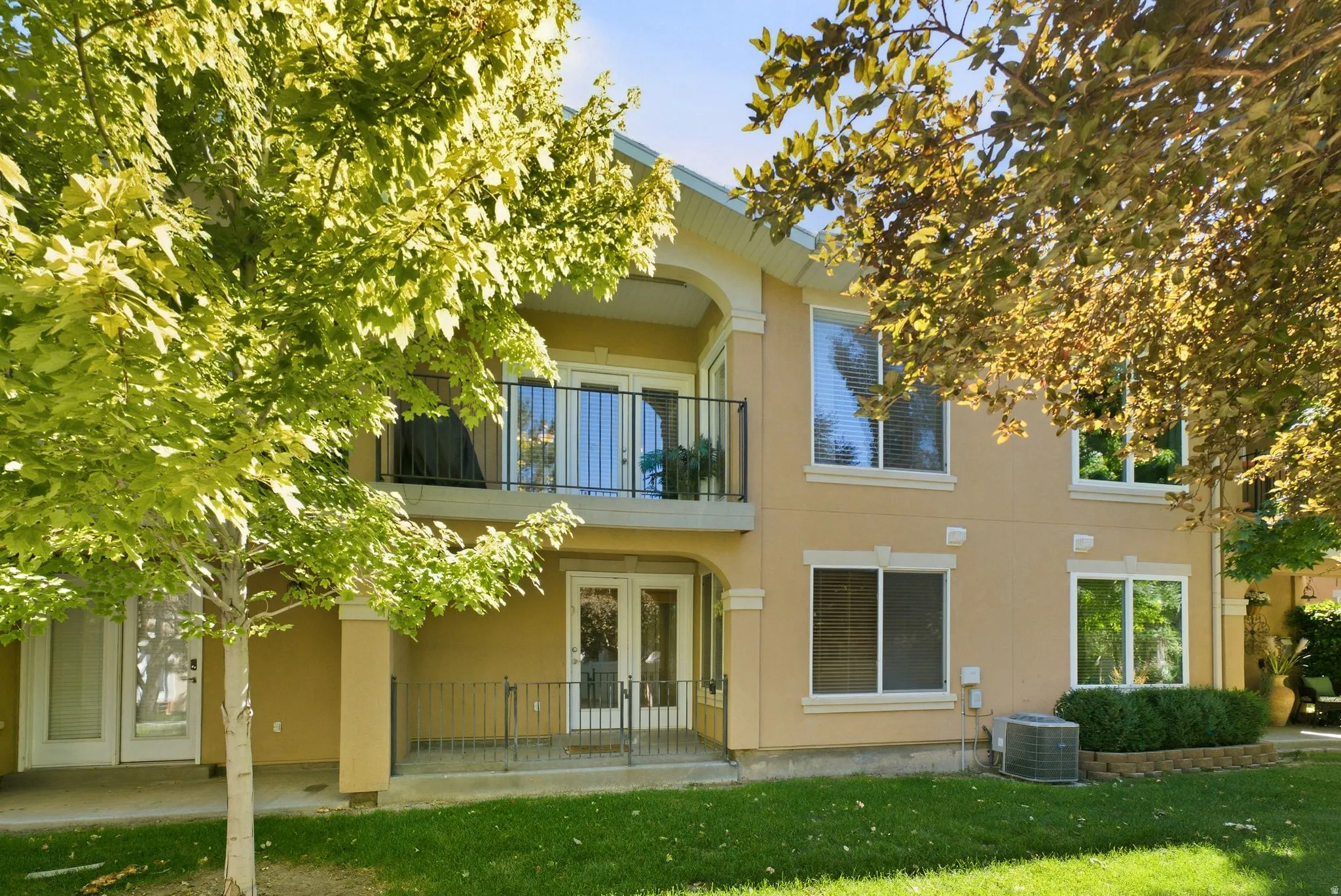 Exterior featuring a stucco finish, multiple windows, a second-story balcony with wrought iron railing, and a ground-level patio