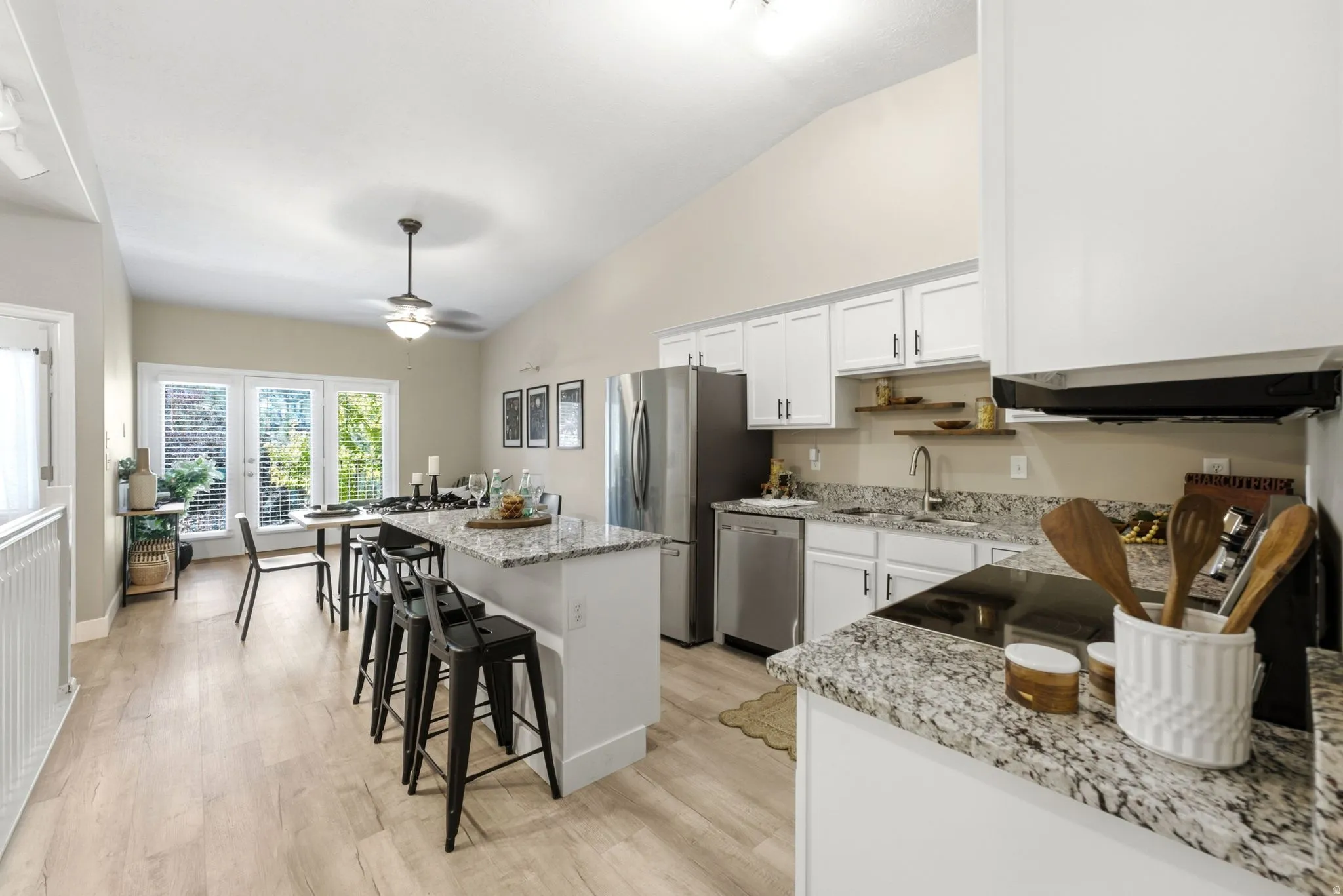 Open-concept kitchen featuring wood-finish flooring, white cabinetry, granite countertops, and stainless steel appliances