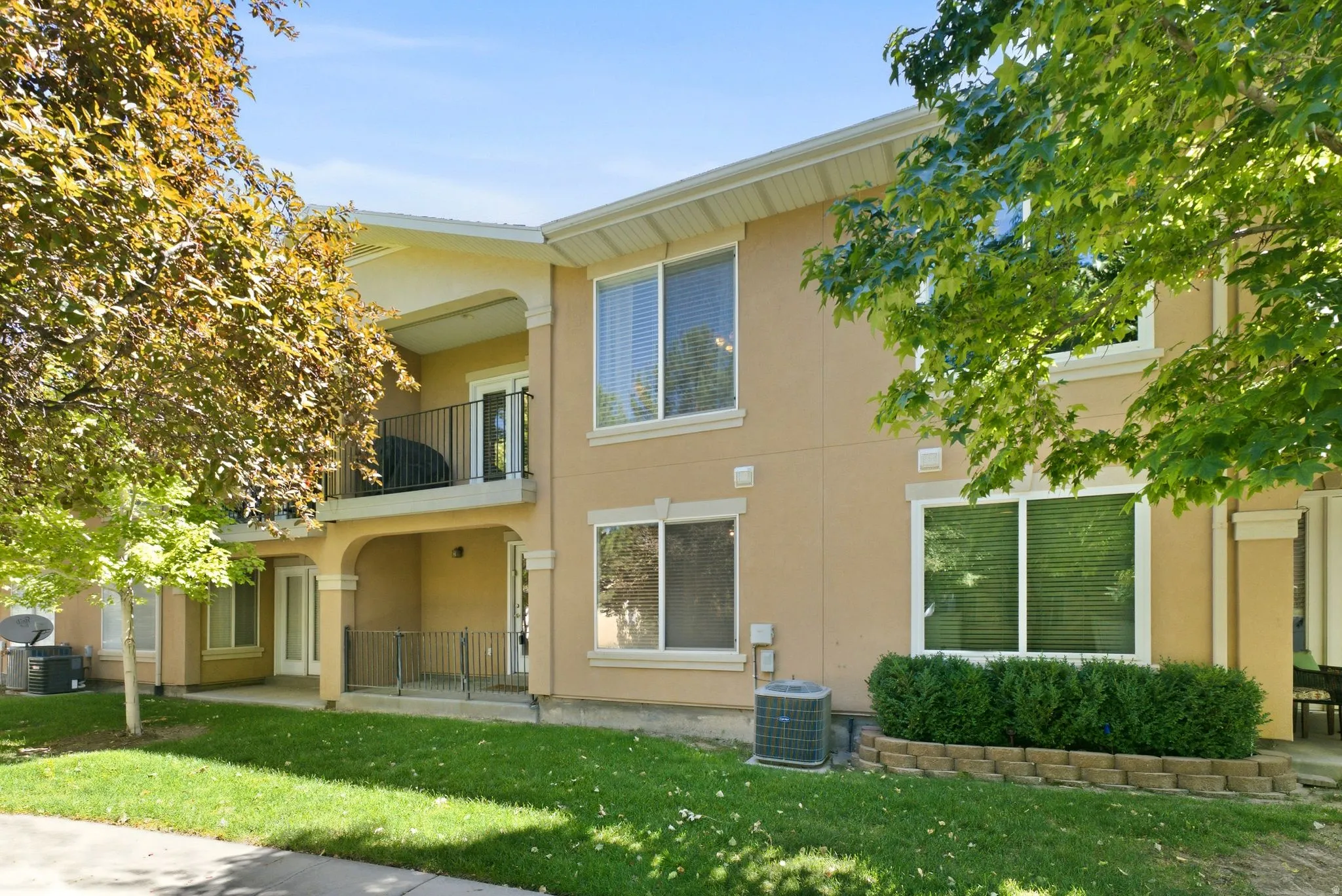 Tan stucco exterior with white-framed windows, a second-story balcony with black railings, and a ground-level covered patio