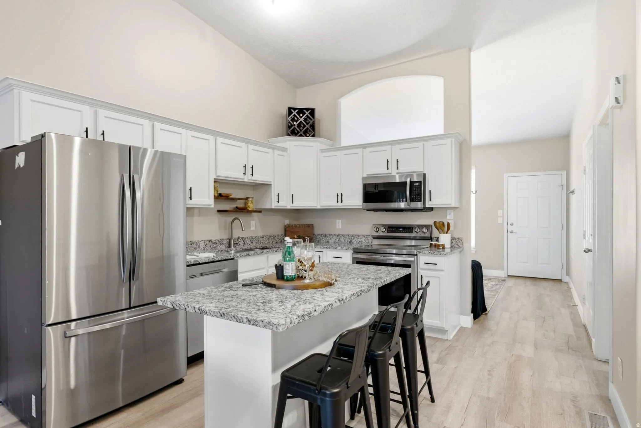 Vaulted ceilings, white shaker cabinetry, stainless steel appliances, speckled countertops, and wood-finish flooring