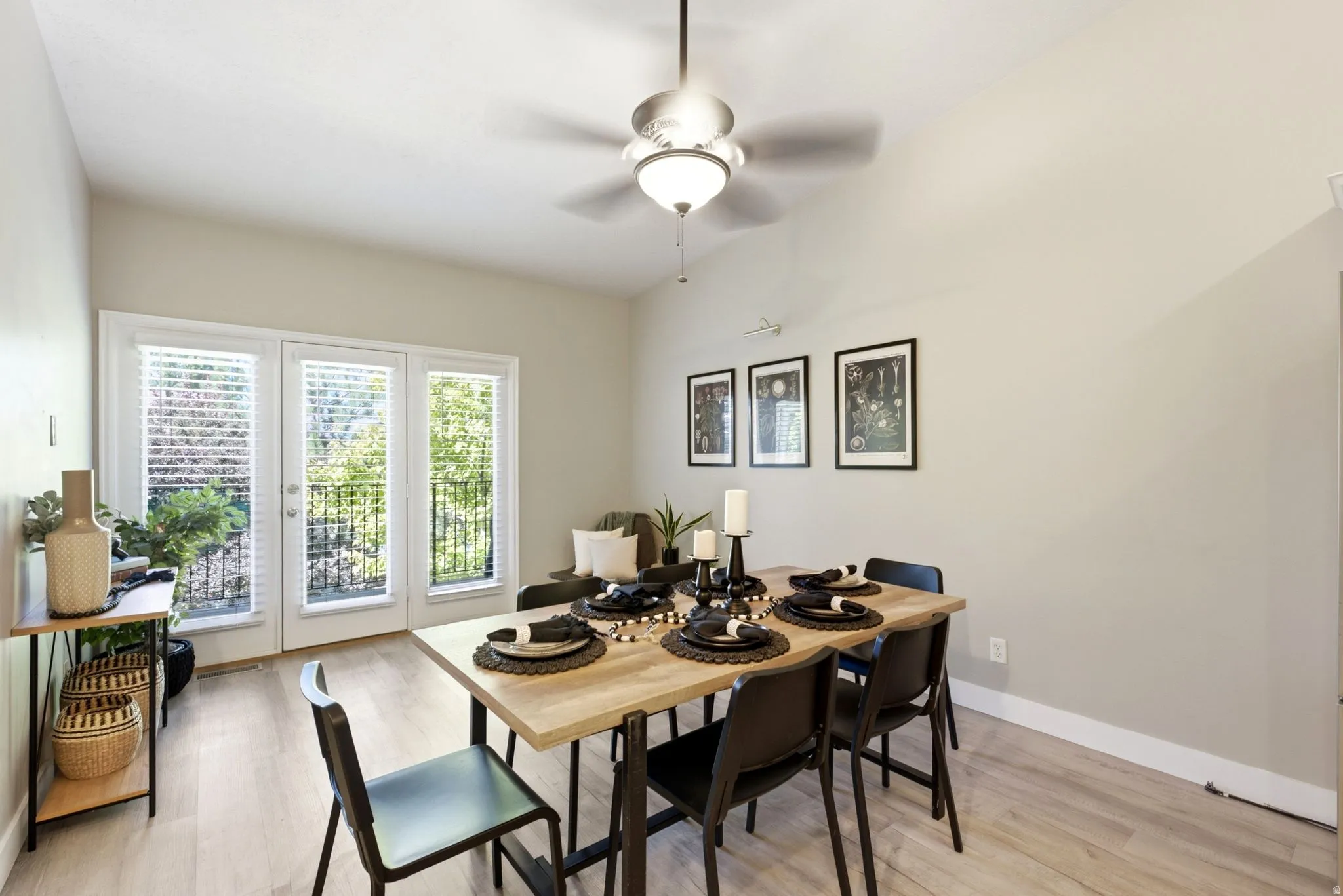 Vaulted ceiling with a ceiling fan light fixture, wood-finish flooring, and multiple glass panel doors providing abundant natural light