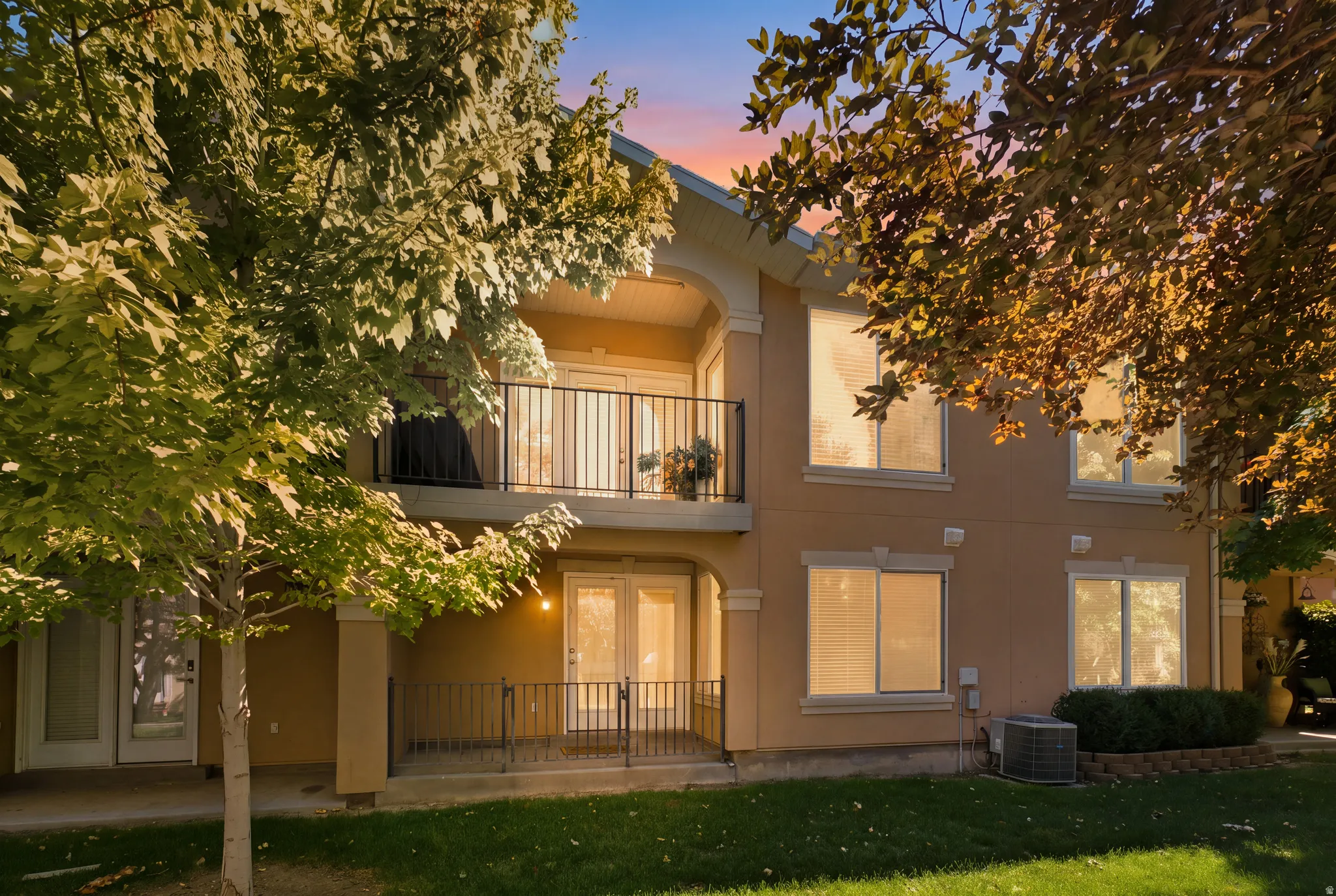 Two-story exterior with a balcony, ground-level patio, multiple windows, and a landscaped perimeter