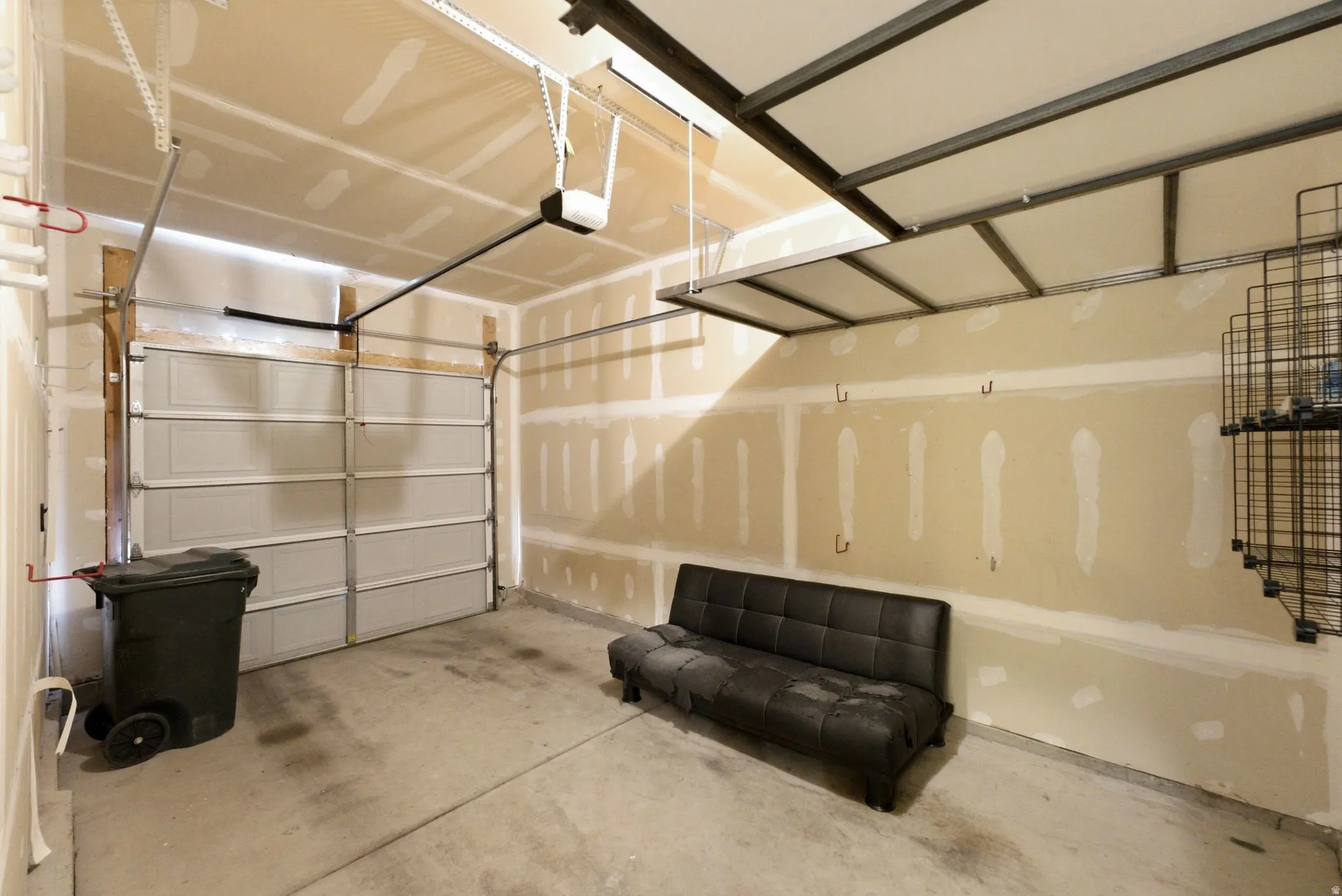 Attached garage with a concrete floor, overhead garage door, built-in overhead storage racks, and wall-mounted storage shelving
