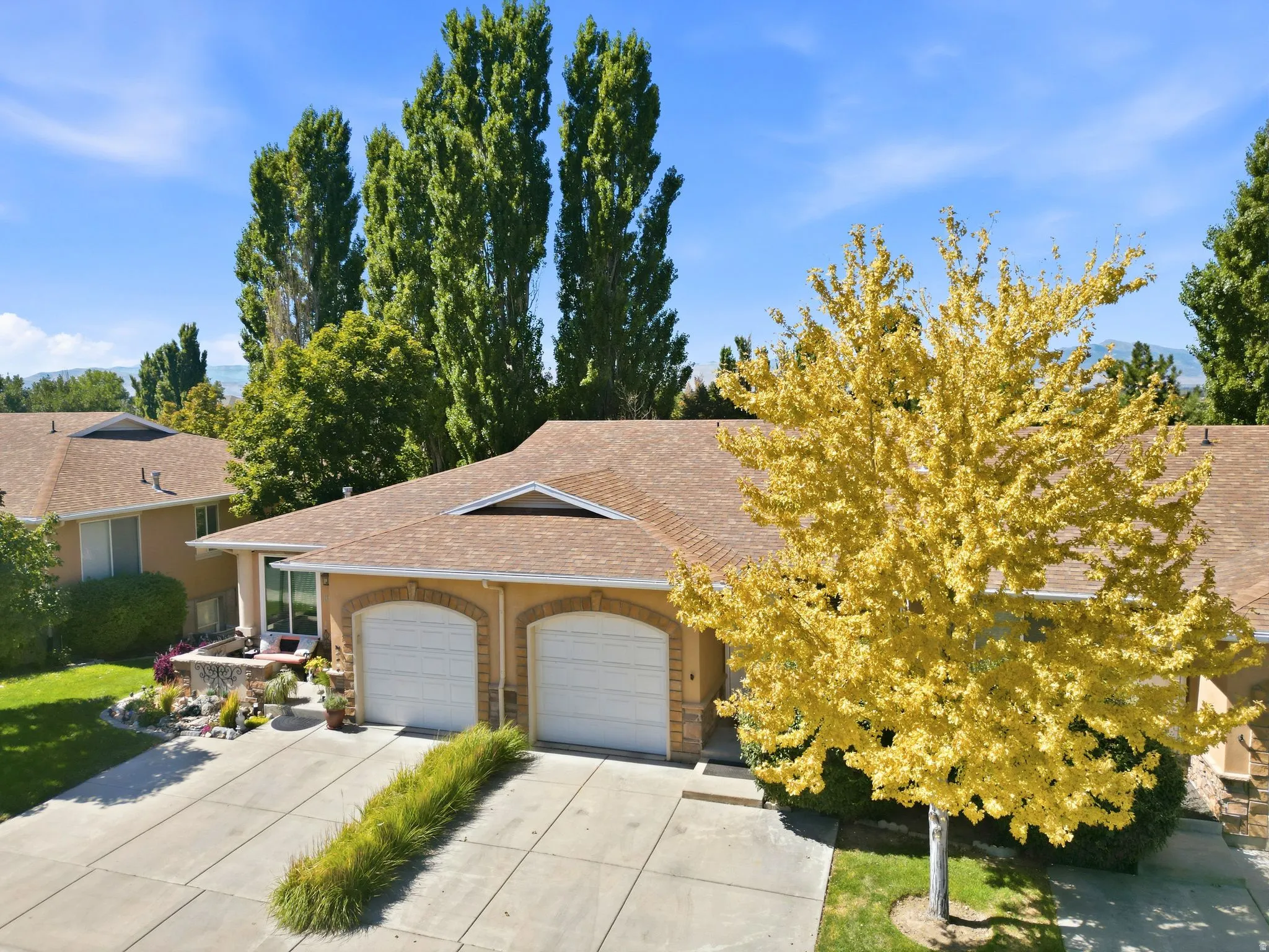 Stucco exterior with arched garage doors, concrete driveway, and mature landscaping