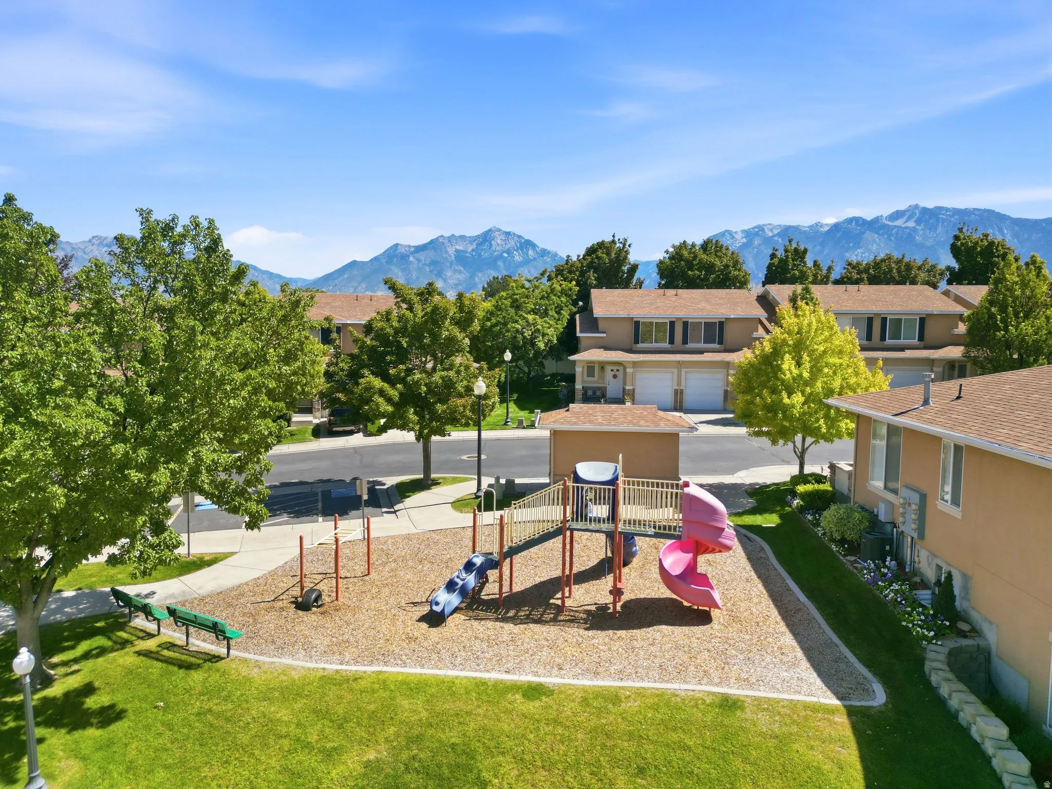 Expansive green lawn with playground area, paved pathways, and mature trees