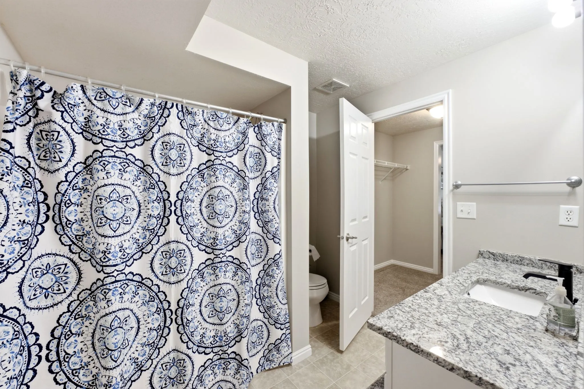 Granite-style countertop with integrated sink and matte black faucet, tile flooring, and a walk-in closet with wire shelving