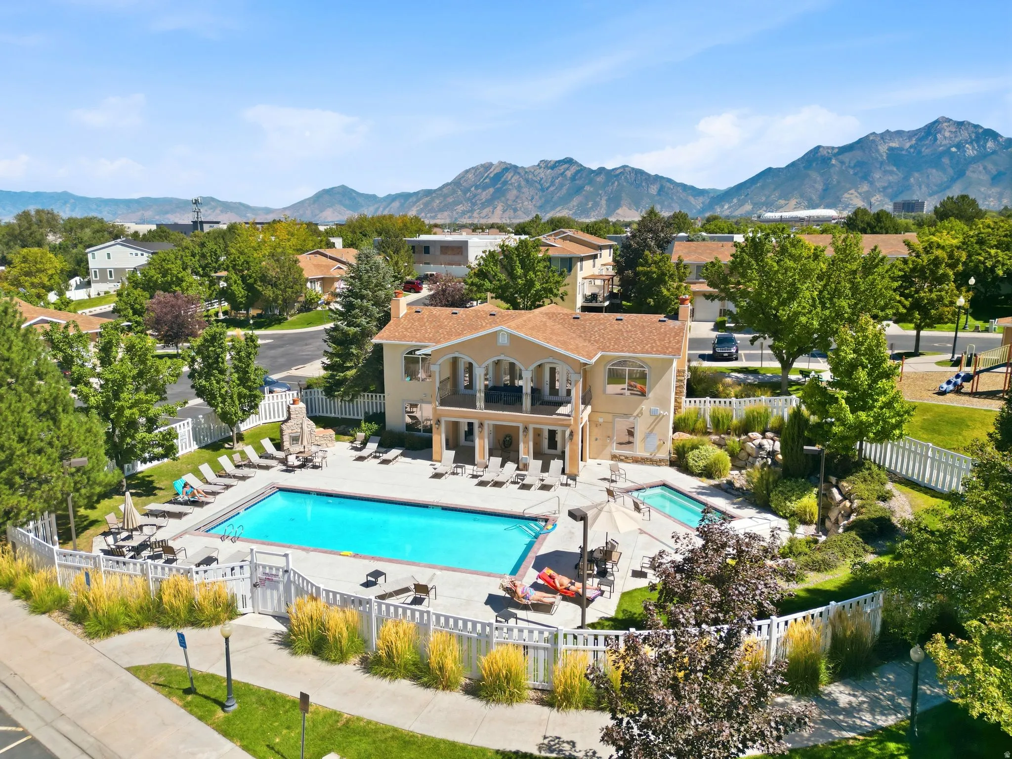 Community pool with surrounding patio, a separate hot tub, fenced perimeter, and nearby playground