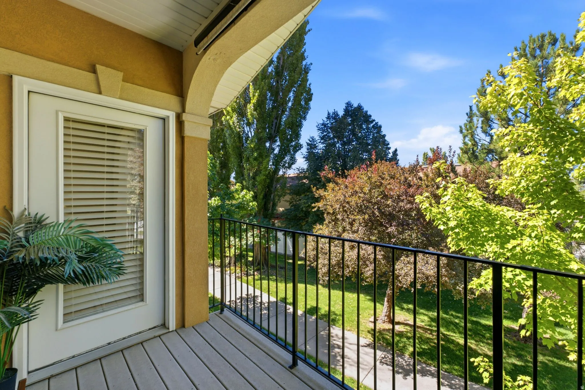 Balcony with composite decking, black metal railing, and a door featuring integrated blinds