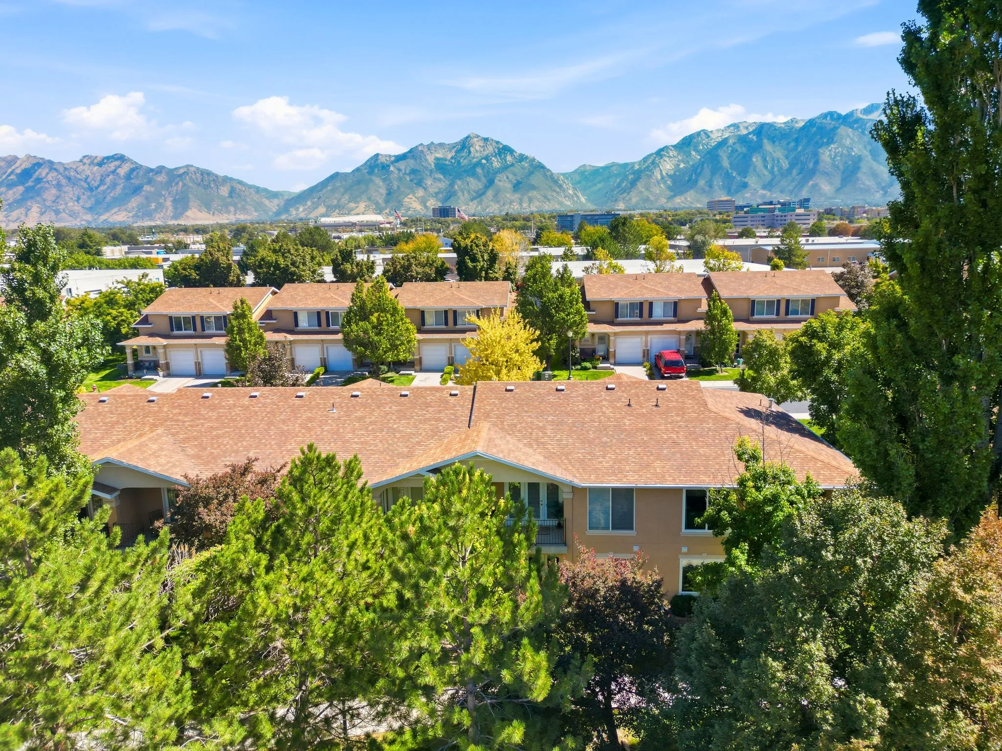 Townhome community with tan exteriors, brown roofs, and integrated garages, surrounded by mature trees