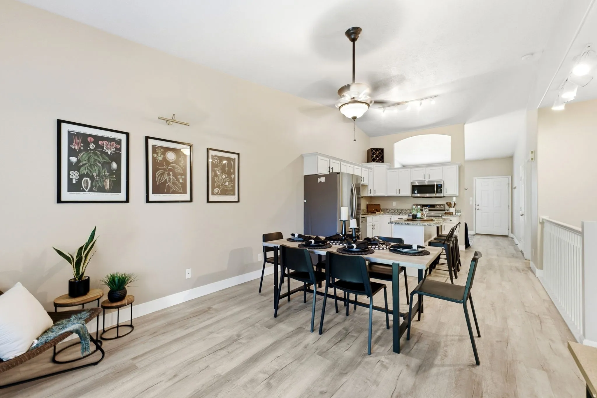 Vaulted ceilings, wood-finish flooring, and a kitchen featuring white cabinetry, stainless steel appliances, and a central island
