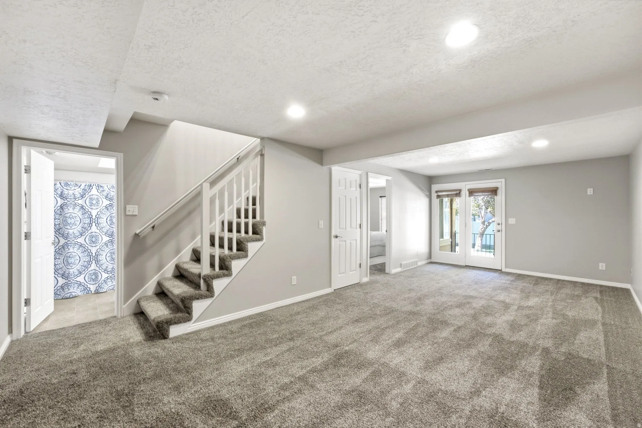 Spacious room with gray carpeting, white trim, and a white staircase with a handrail
