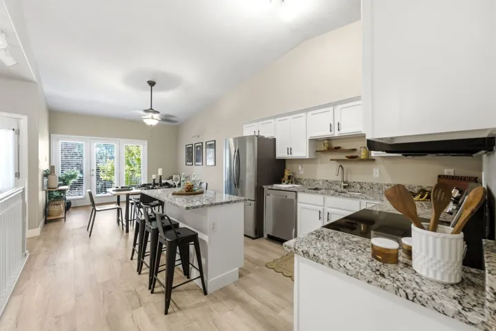 Open-concept kitchen featuring wood-finish flooring, white cabinetry, granite countertops, and stainless steel appliances