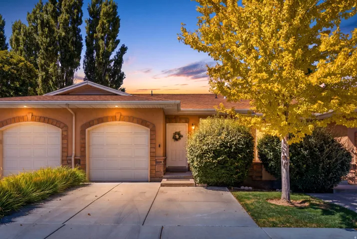 Stucco exterior with stone accents, arched garage doors, concrete driveway, and established landscaping