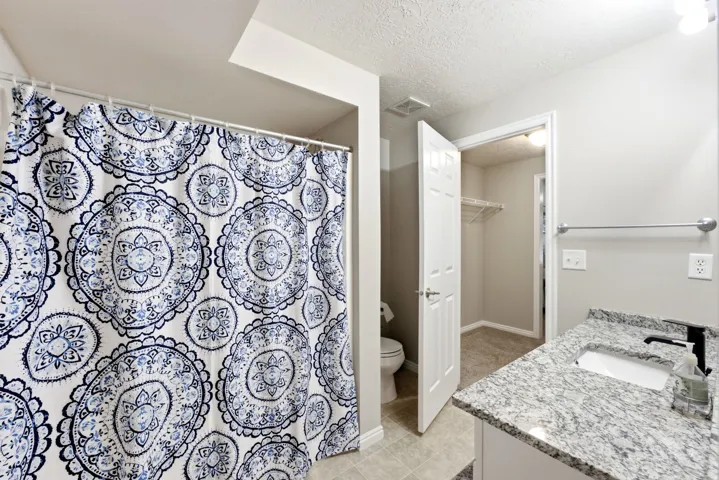 Granite-style countertop with integrated sink and matte black faucet, tile flooring, and a walk-in closet with wire shelving