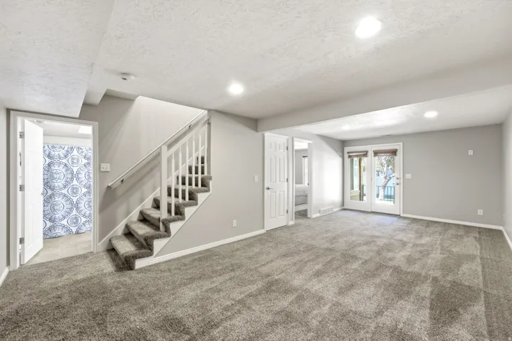 Spacious room with gray carpeting, white trim, and a white staircase with a handrail