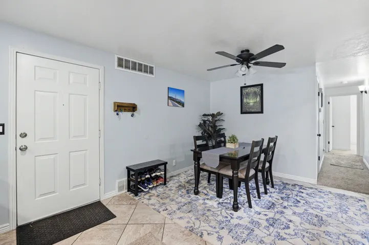 Tiled entryway with a paneled door, leading to an open dining area with a ceiling fan