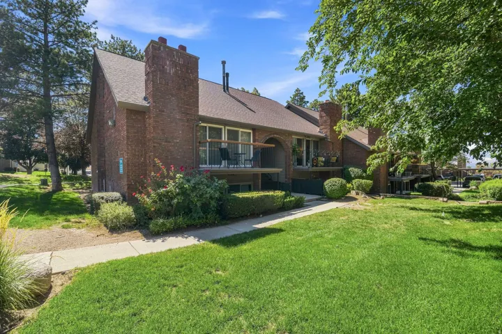 Brick exterior with multiple chimneys, mature landscaping, sidewalk access, and private balconies