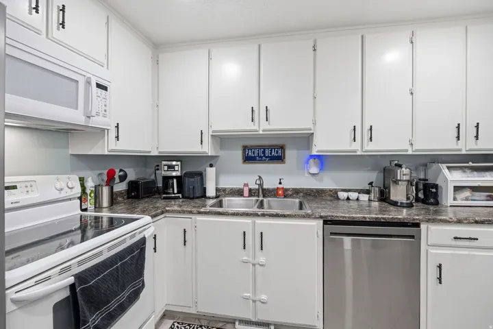 White cabinetry, laminate countertops, dual basin stainless steel sink, stainless steel dishwasher, and white electric range