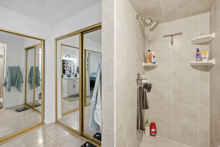 Mirrored closet doors with gold-tone frames, tile flooring, and a tiled shower with a wall-mounted showerhead