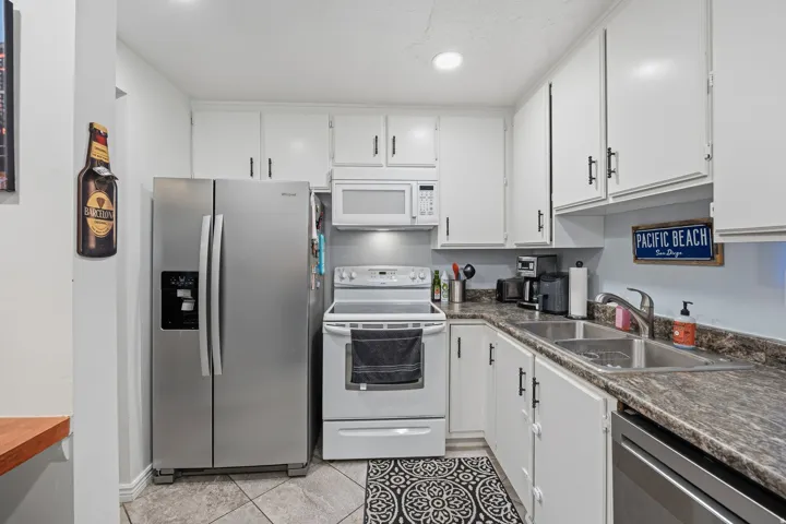Kitchen featuring white cabinetry, stainless steel appliances, a double basin sink, solid surface countertops, and tile flooring