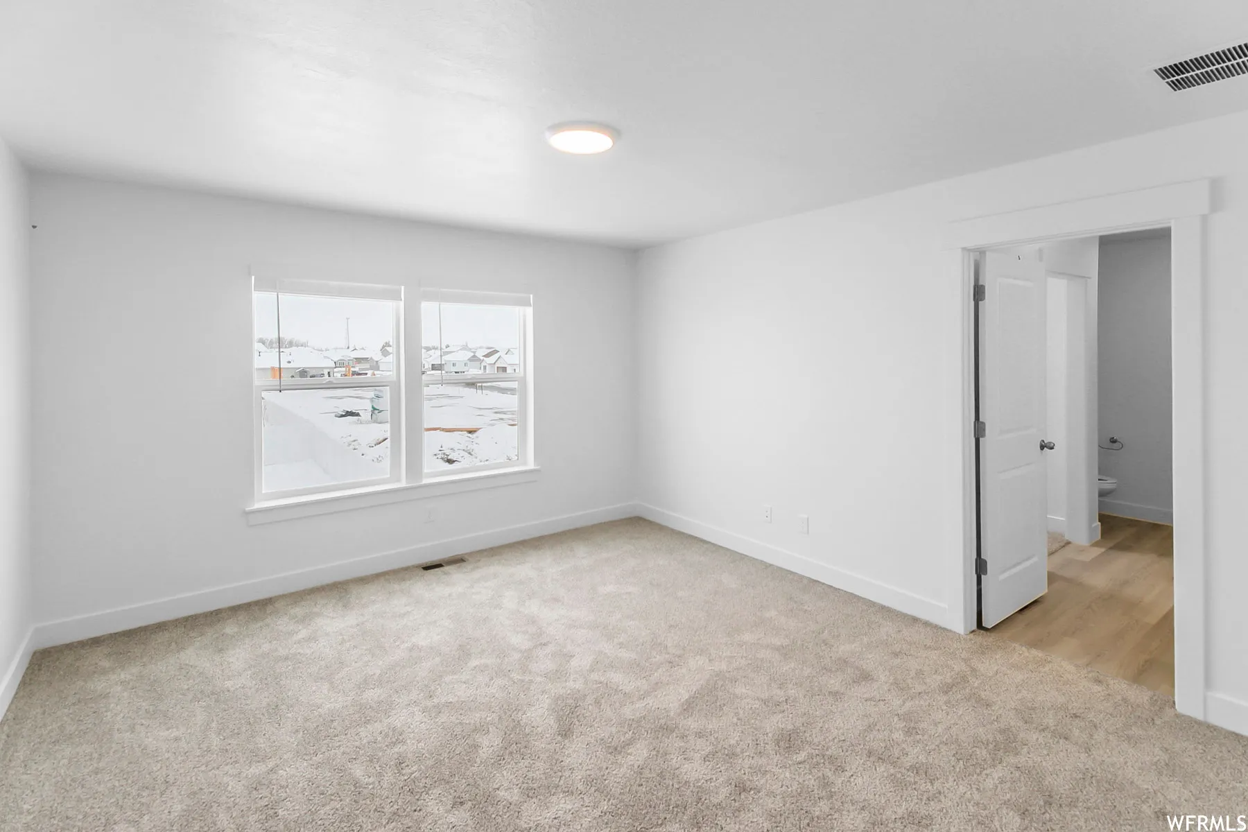 Dual windows with white trim, recessed ceiling light, and light-colored carpeting