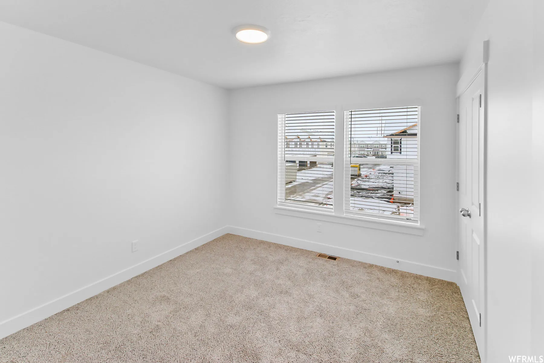 Carpeted room featuring a ceiling-mounted light fixture, dual windows with blinds, and white trim