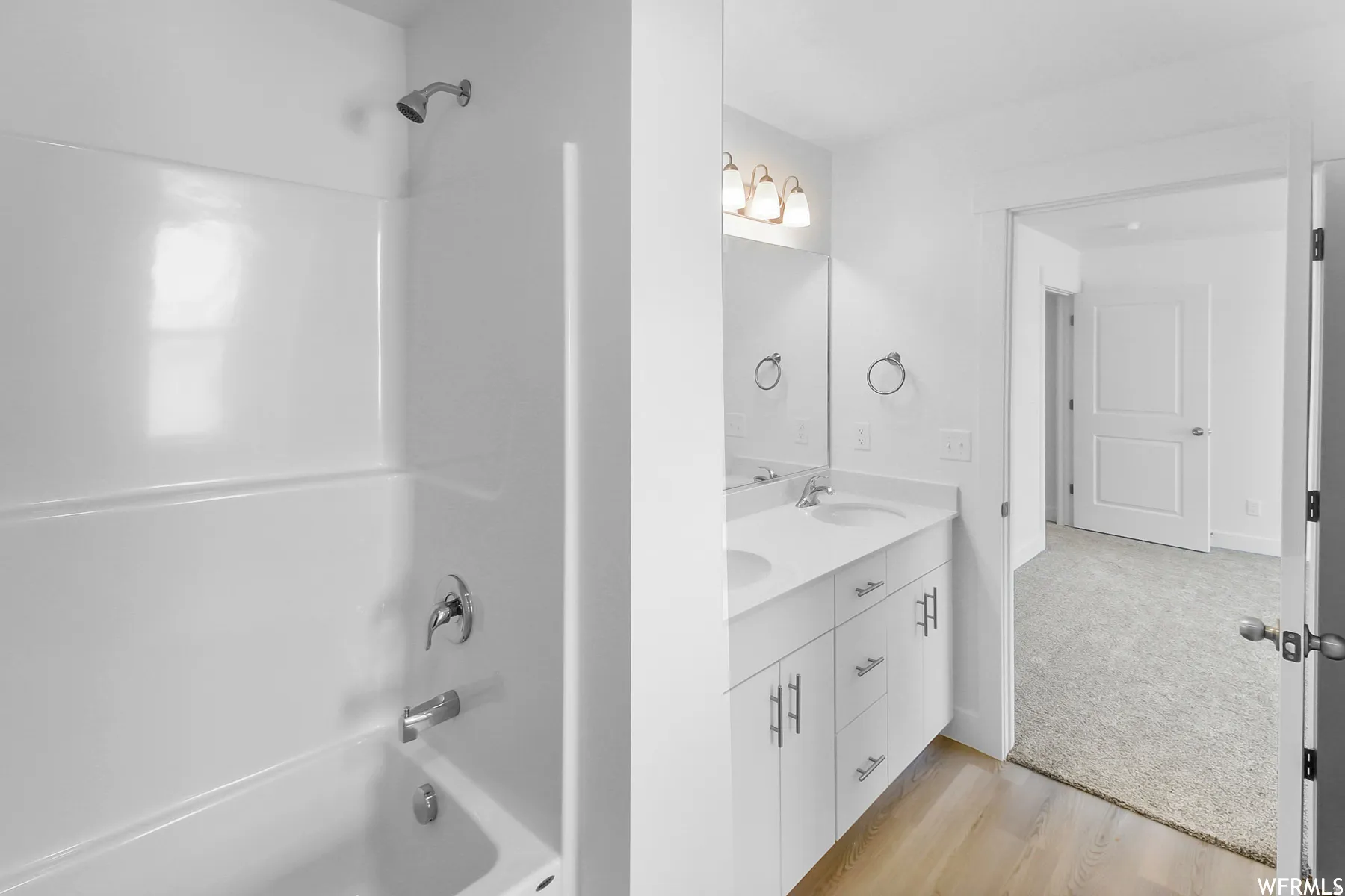 White dual vanity with integrated sinks, chrome fixtures, and wood-finish flooring