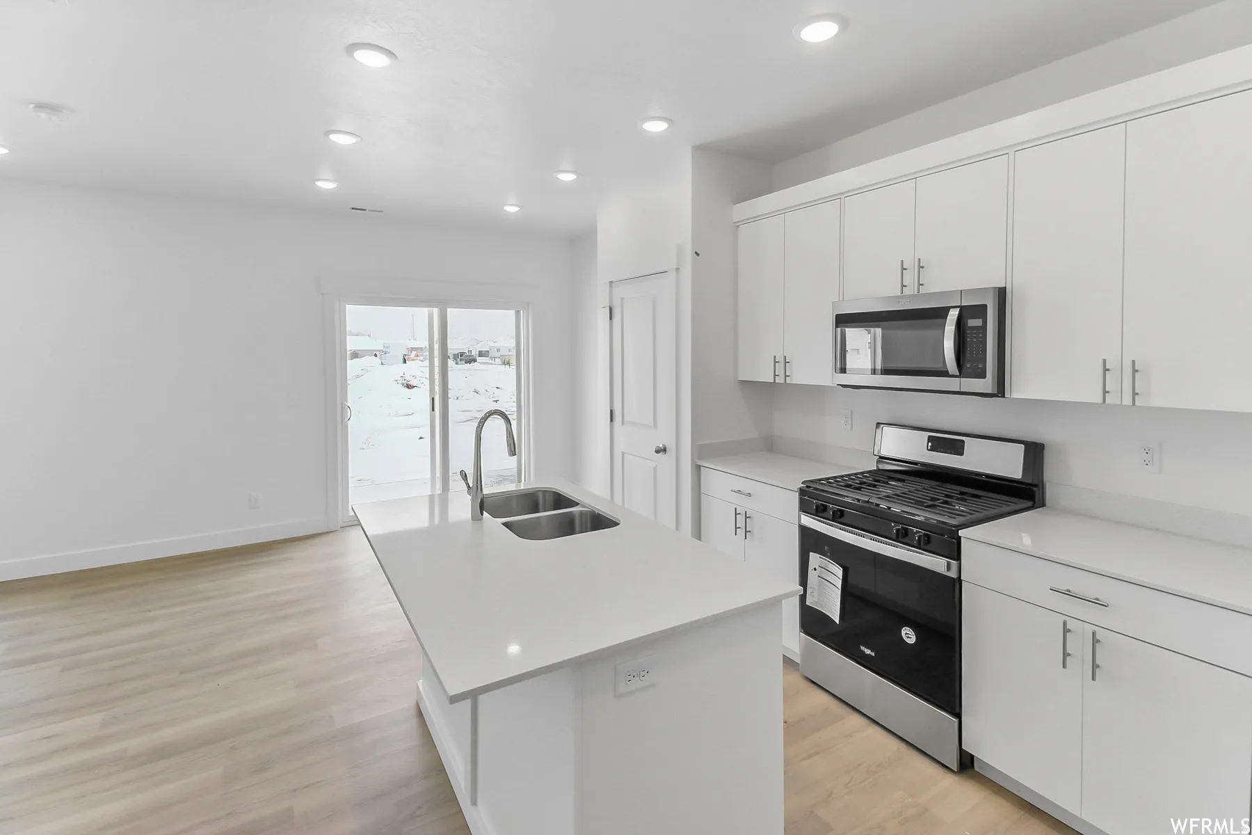 Kitchen featuring an island with a double basin sink, white cabinetry, a stainless steel gas range, and a built-in microwave