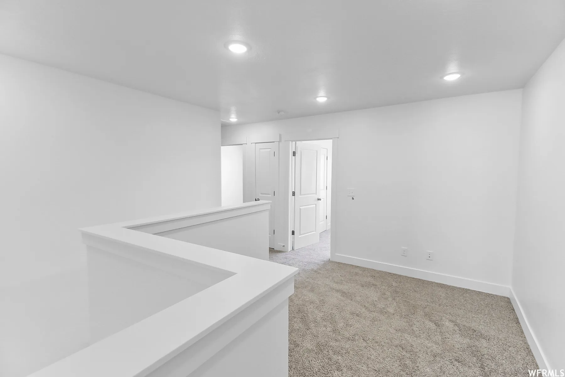 Recessed lighting, light-toned carpeting, white walls, white trim, and a white interior railing