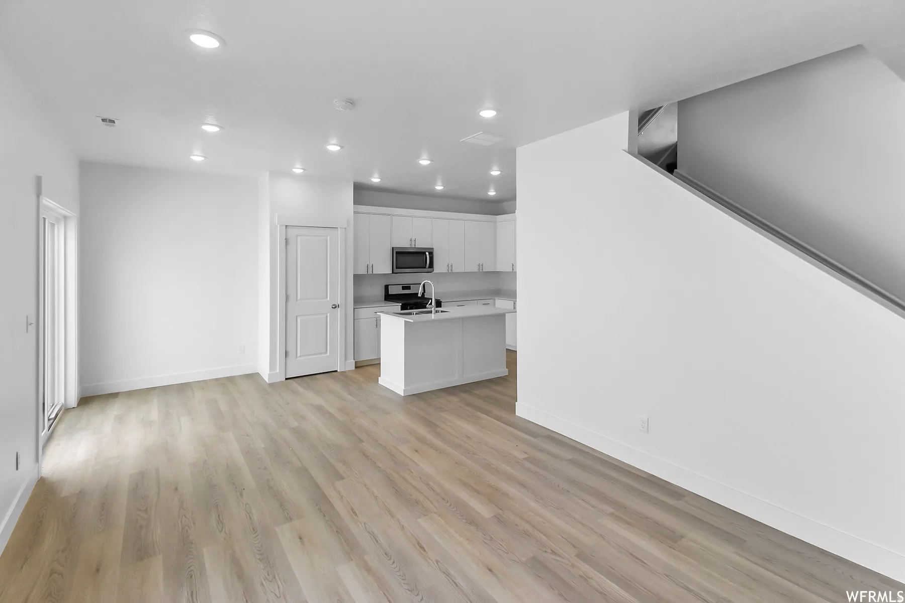 Open-concept living space featuring wood-finish flooring, recessed lighting, and a modern kitchen with white cabinetry