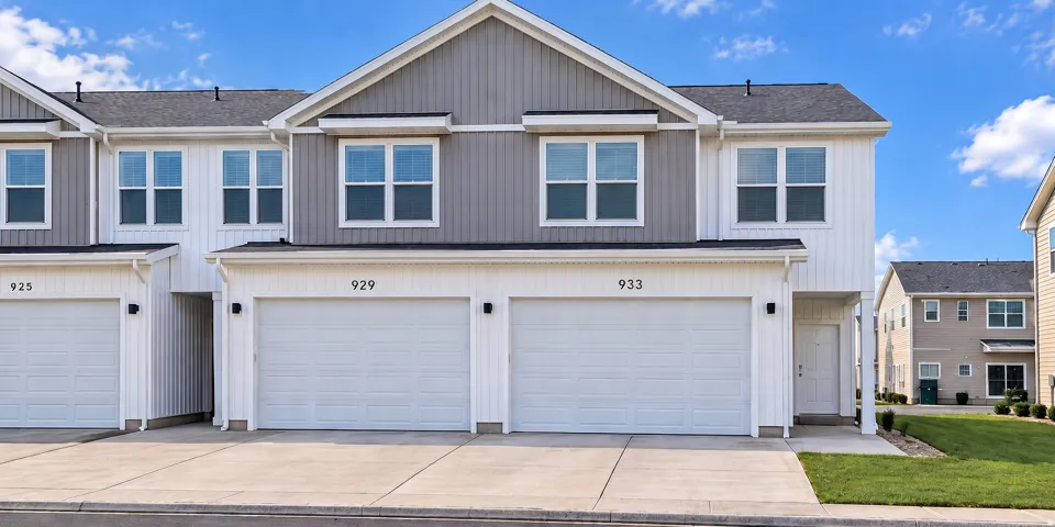 Modern townhome exterior with light gray and white siding, attached garages, and a paved driveway