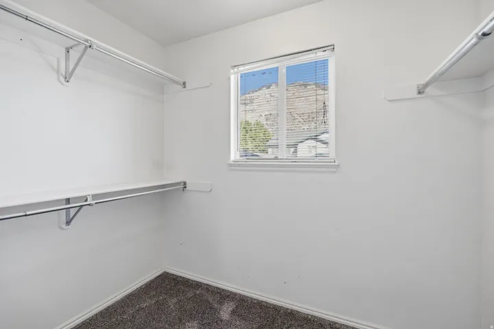 Built-in closet shelving and hanging rods with a window featuring horizontal blinds