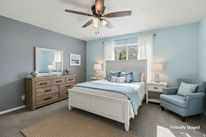 Virtually staged Primary Bedroom. Carpeted flooring throughout, ceiling fan with integrated lighting, and a window with white sheer curtains