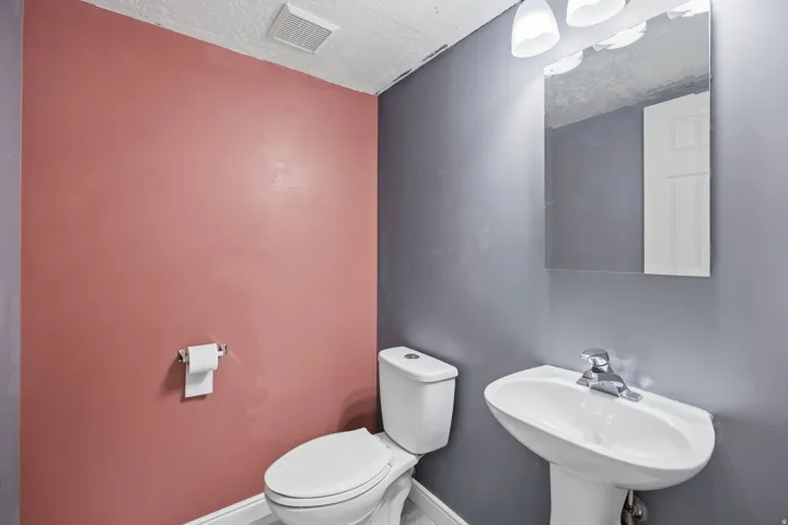 Pedestal sink with chrome faucet, wall-mounted mirror, and overhead vanity lighting