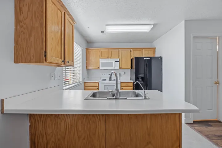 Kitchen featuring wood cabinetry, white countertops, a double basin stainless steel sink, and a black refrigerator