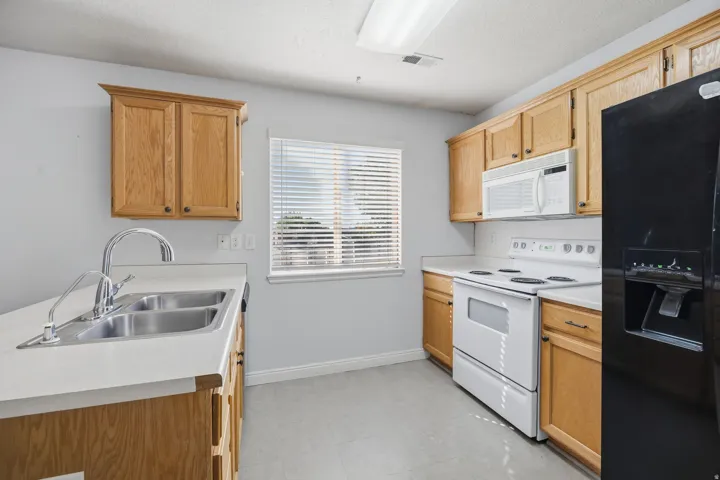 Light wood-finish cabinetry, white countertops, stainless steel double basin sink, white range, and black refrigerator