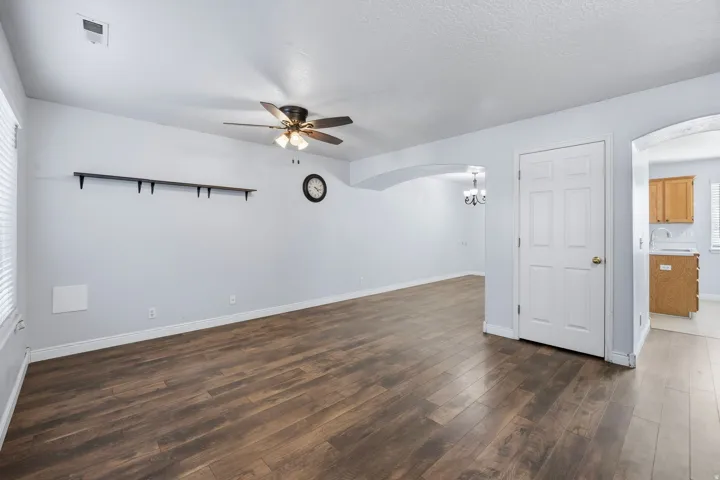 Wood-finish flooring throughout, ceiling fan with integrated lighting, arched entryway, and white paneled interior door