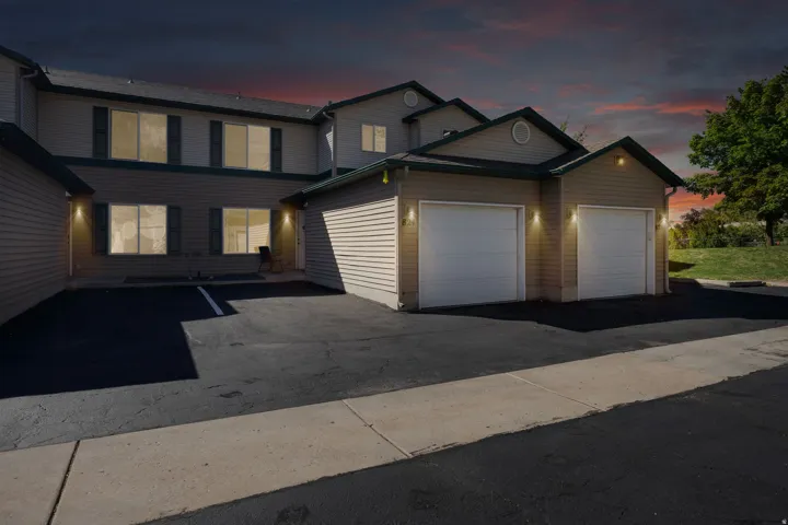 Townhouse property with a multi-car paved parking area, one attached single-car garage, horizontal siding, and multiple windows with dark shutters