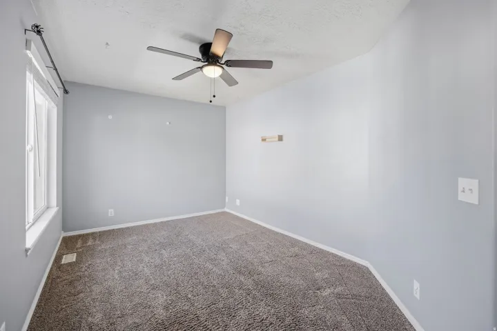 Sloped ceiling with a ceiling fan light fixture, light gray wall paint, and textured carpeting