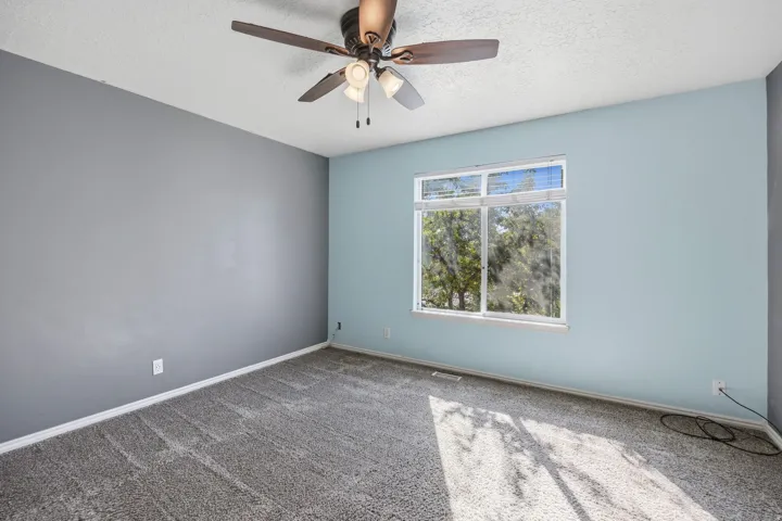 Window with outdoor scenery, ceiling fan with integrated lighting, textured ceiling, and gray carpeting