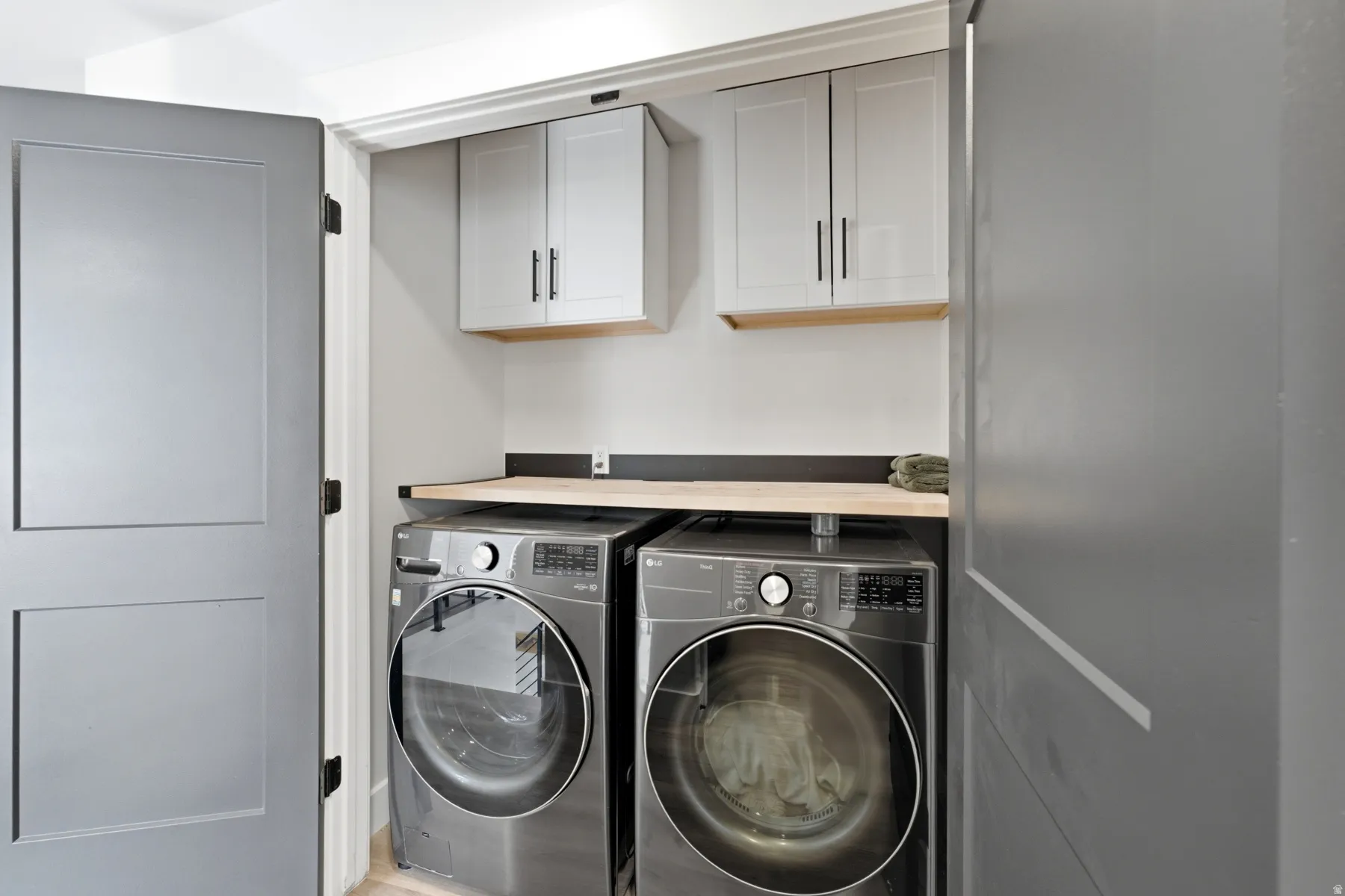 Dedicated laundry area featuring a light wood finish countertop, two upper cabinets with black hardware, and two front-loading machines