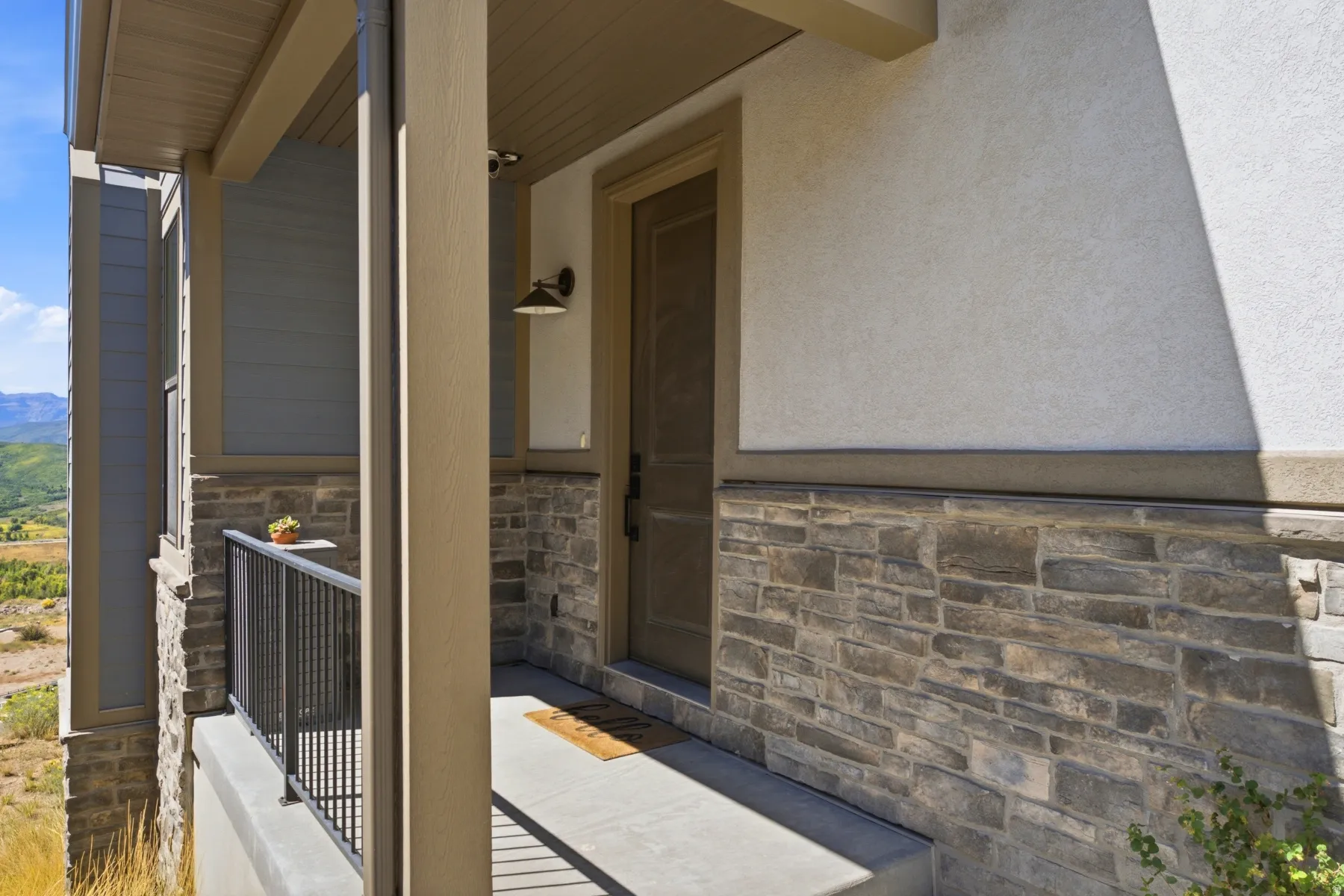 Entryway featuring stone facade, stucco exterior, covered porch, and mountain backdrop