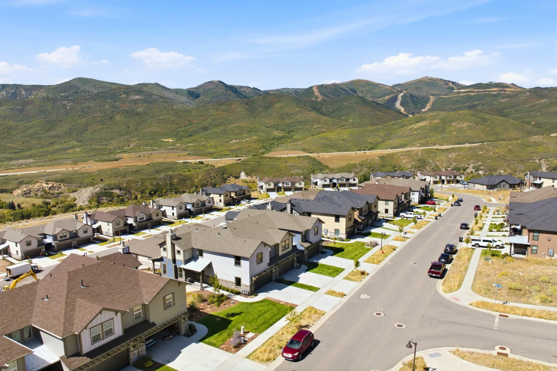 Residential neighborhood with paved streets and sidewalks, featuring multiple single-family homes with varying exterior finishes, against a backdrop of natural mountainous terrain
